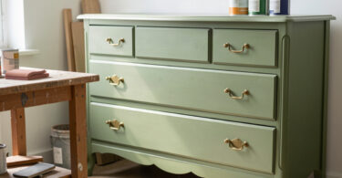 Commode vintage relookée en peinture vert sauge dans un atelier créatif lumineux, illustrant la tendance du surcyclage de meubles
