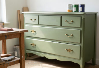 Commode vintage relookée en peinture vert sauge dans un atelier créatif lumineux, illustrant la tendance du surcyclage de meubles